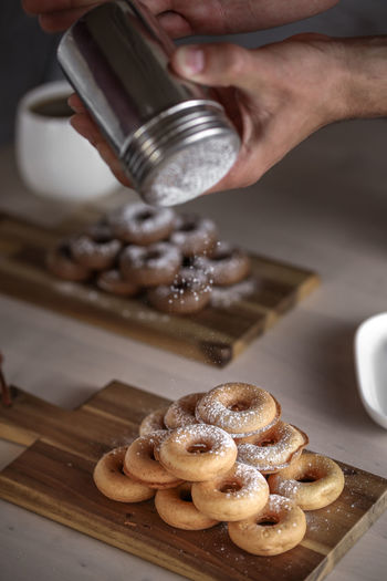 Cropped image of man dusting powdered sugar on donuts in kitchen