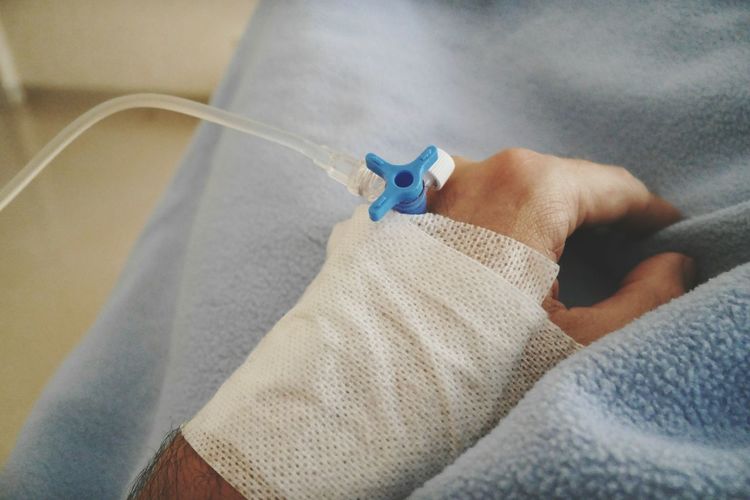 Cropped hand of patient with iv drip on bed