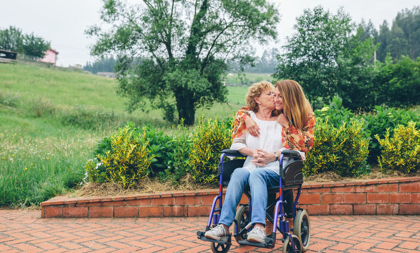Mother kissing daughter while sitting on wheelchair in public park