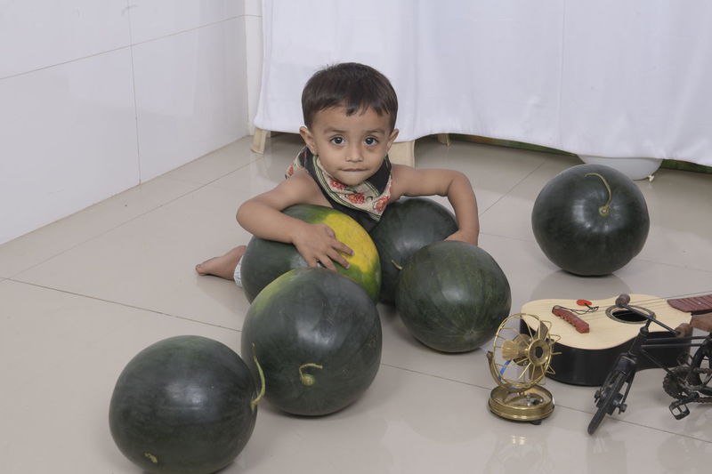 Portrait of boy sitting on floor at home holding watermelon