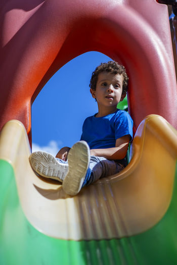 Beautiful caucasian curly haired boy, in playground sitting on top of a slide