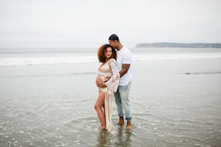 Mixed race couple posing on beach, maternity