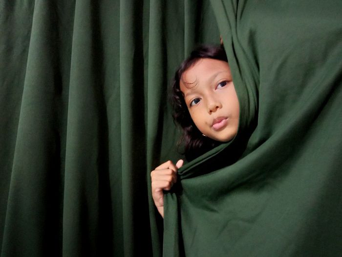 Portrait of girl hiding behind curtain