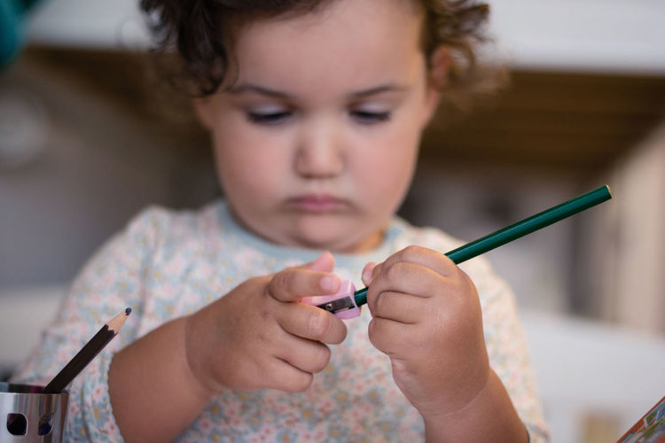 Low angle view of cute girl sharpening pencil while sitting at home