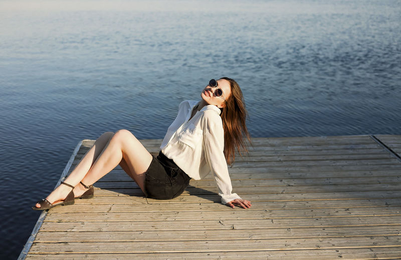 Young woman sitting on pier near sea