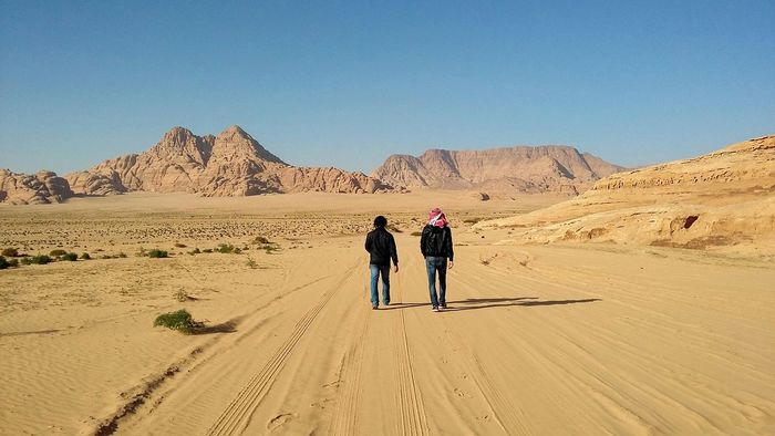 Rear view full length of friends walking in desert against sunny day
