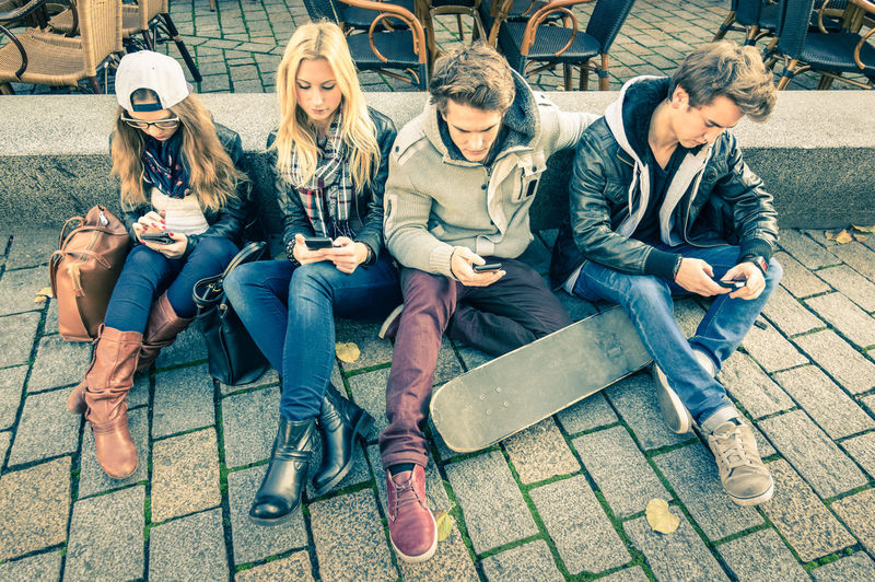 Full length of friends sitting on mobile phone in city