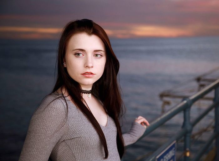 Beautiful young woman standing against sea during sunset