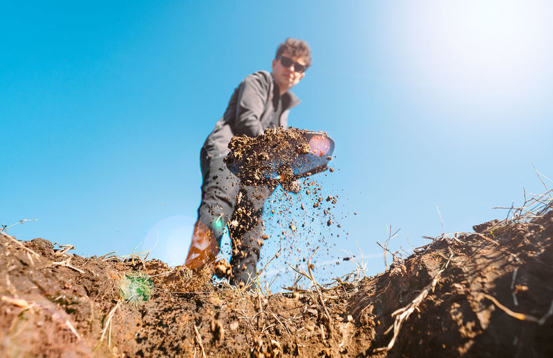 Low angle view of a young man digging a hole in the ground. man using shovel