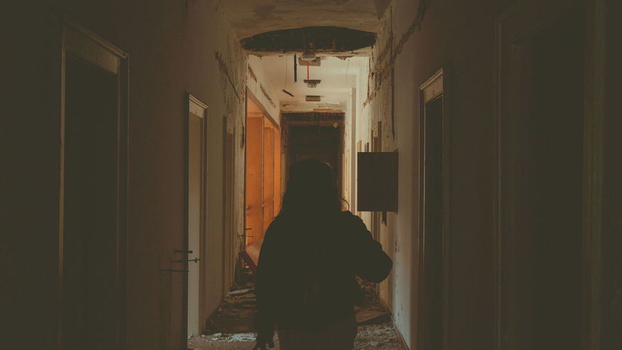 Rear view of woman standing in corridor of abandoned house