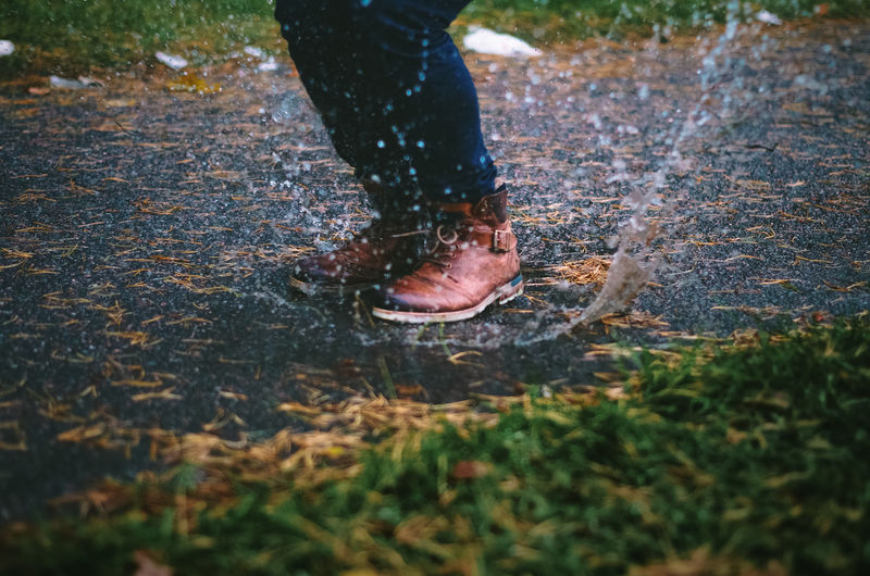 Low section of person jumping in puddle