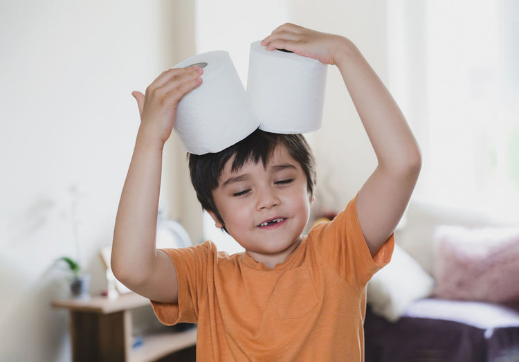 Cute boy holding toilet paper roll at on head at home