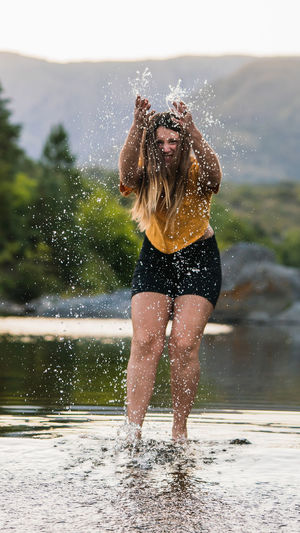 Full length portrait of woman splashing water while standing in lake