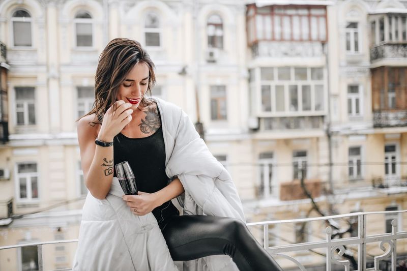 Woman having red wine while wrapped in blanket at balcony