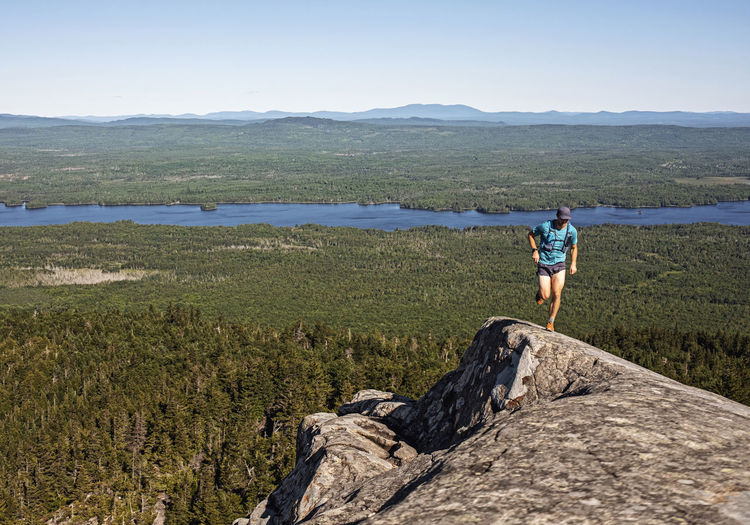 Male runner on mountaintop peak in maine woods.