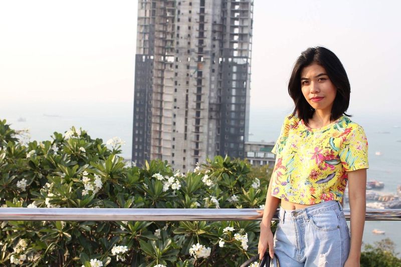 Portrait of young woman standing by railing against skyscraper