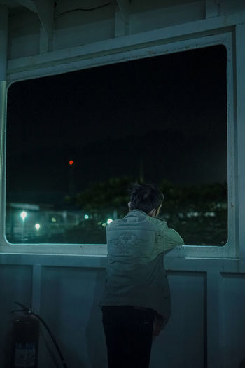 Rear view of woman standing by window at night