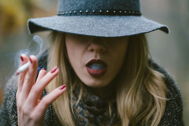 Close-up of woman in hat smoking cigarette