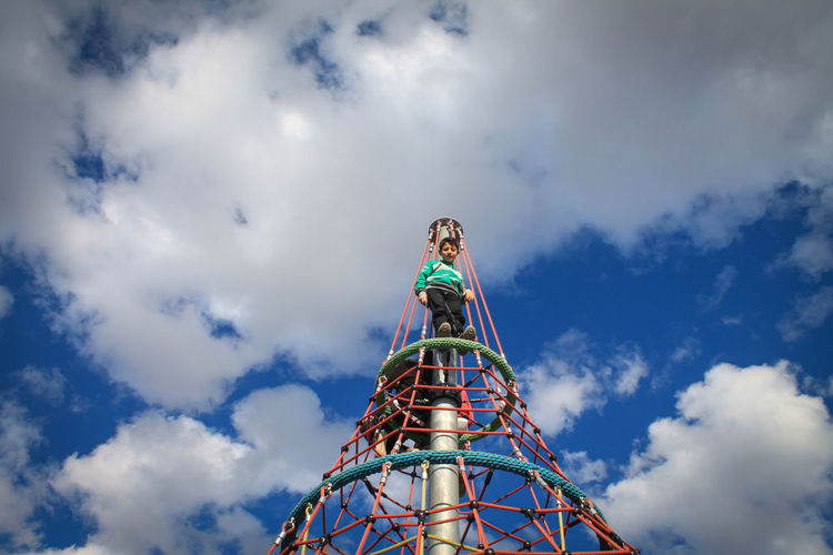 Low angle view of boy standing on play equipment against sky