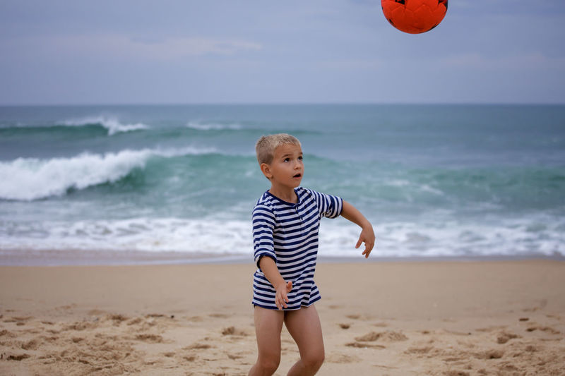 Playful boy playing with ball at beach