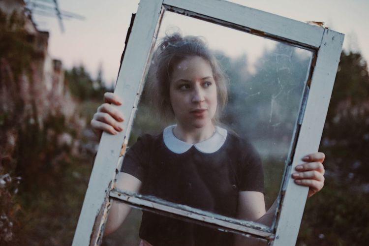Portrait of young woman holding window while standing outdoors