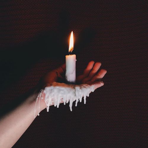 Close-up of woman hand holding lit candle against black background