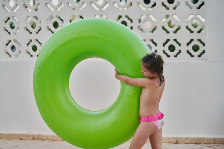 Girl carries a green float in her arms by the pool