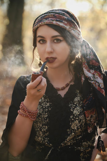 Portrait of beautiful young woman smoking pipe while sitting outdoors