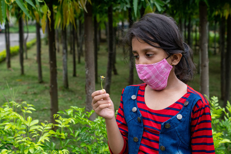 Portrait of girl with pink face mask looking at flower