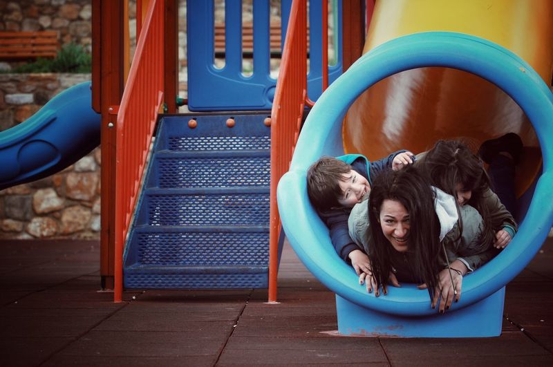 Portrait of happy mother with children in slide at playground