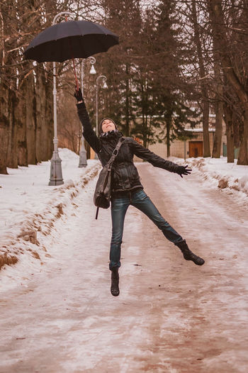 A girl jumps with an umbrella in the park. in winter, a person flies up, hanging in the air