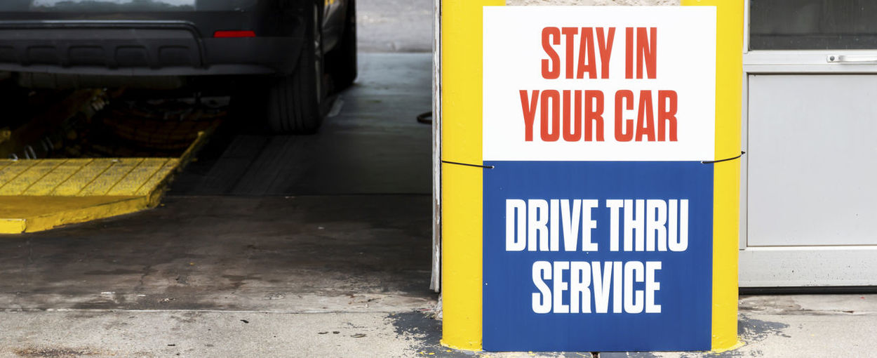 An automotive service center with a sign reading to stay in your car for drive through service.