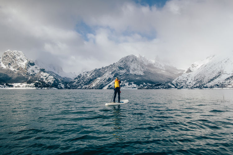 Tourist floating on sup between water surface and picturesque view of hills in snow