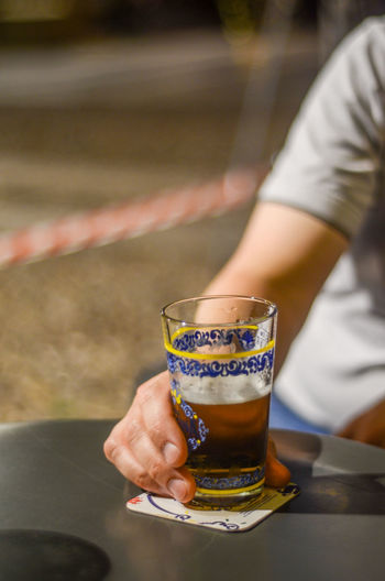 Midsection of man holding drink glass of cold beer