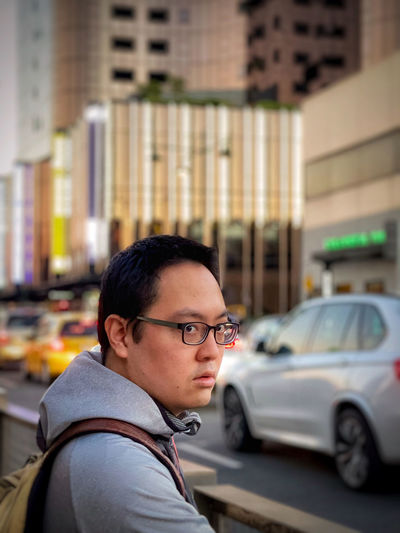 Portrait of young man on pavement against busy street and skyscrapers in city.