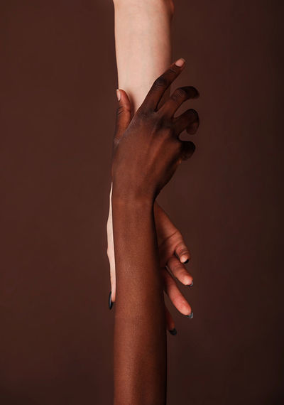 Cropped multi-ethnic women holding hands against brown background