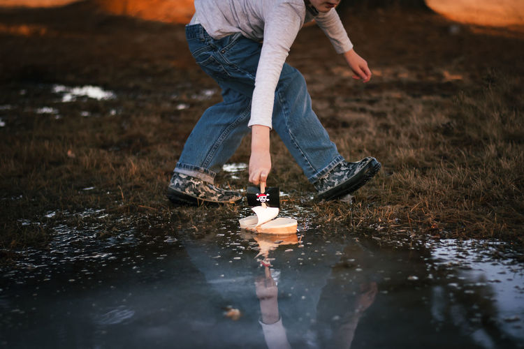 A young boy playing with a toy boat in a puddle of water