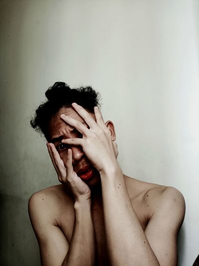 Portrait of shirtless young man covering face against wall