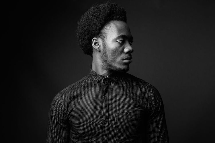 Portrait of young man standing against black background