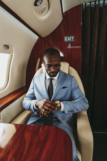 Male entrepreneur checking time on wristwatch while traveling in private jet