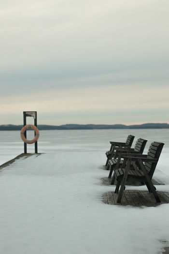  bench at snowed shore against sky