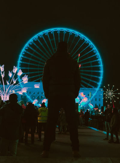 Silhouette man standing against illuminated ferris wheel at night
