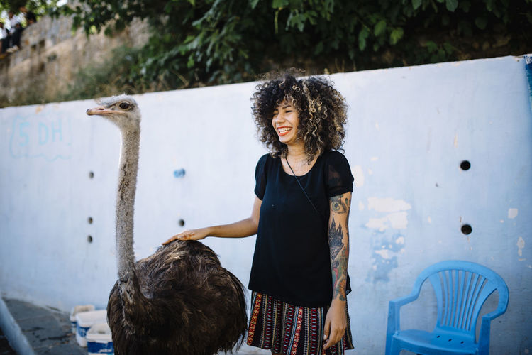 Happy woman with ostrich standing against the wall
