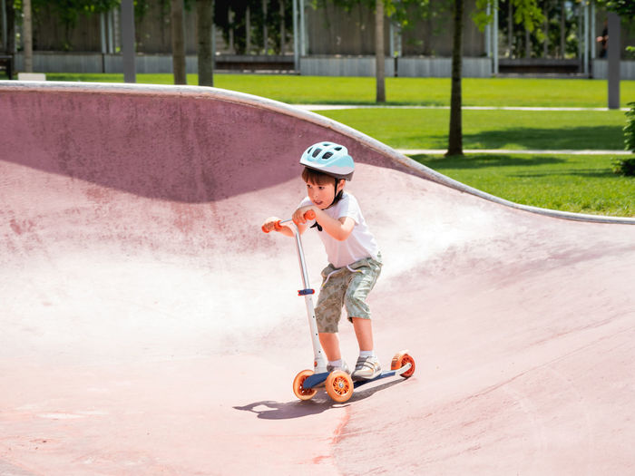 Little boy rides kick scooter in skate park. special concrete bowl structures in urban park. 