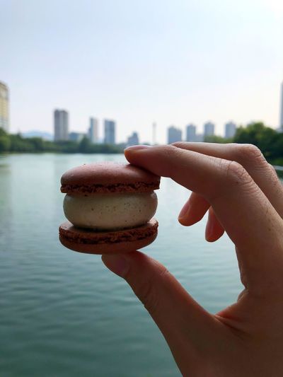 Close-up of hand holding macaroon against sky