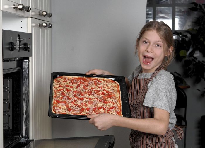 A teenager in an apron enthusiastically puts a pizza pan in the kitchen oven. healthy home cooking. 