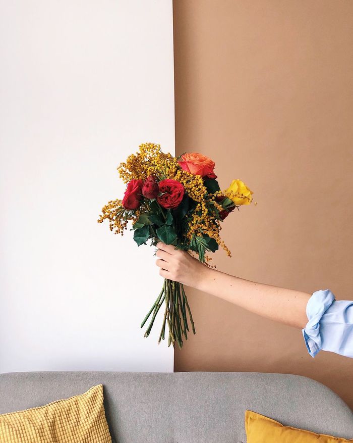 Cropped hand of hand holding bouquet against wall