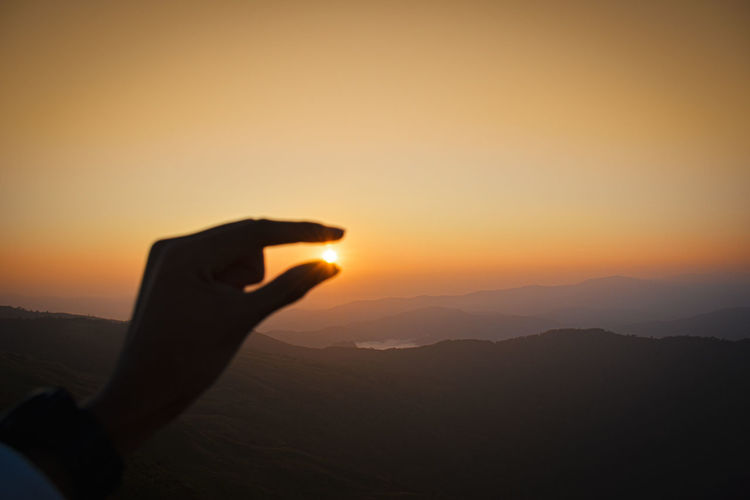 Silhouette hand against orange sky during sunset