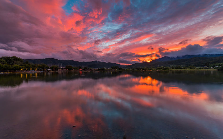 Scenic view of lake against dramatic sky during sunset