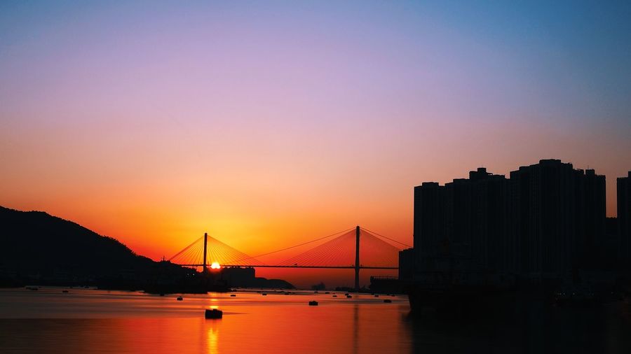 Silhouette bridge over bay against sky during sunset